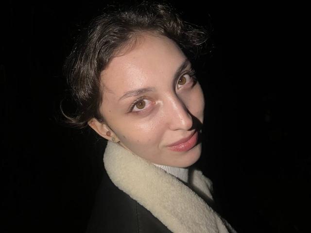 LeonieRahim has short, wavy brown hair, light skin, and brown eyes. She's wearing a black coat with a white fur collar, smiling slightly with a shiny nose.