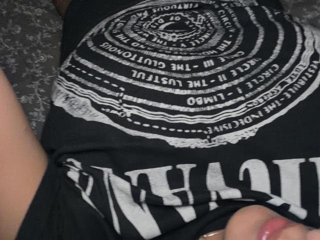 SarahPrincess's black shirt with white circular text and fringed edges, showing her black and white striped pants, and her right hand with pink nail polish.