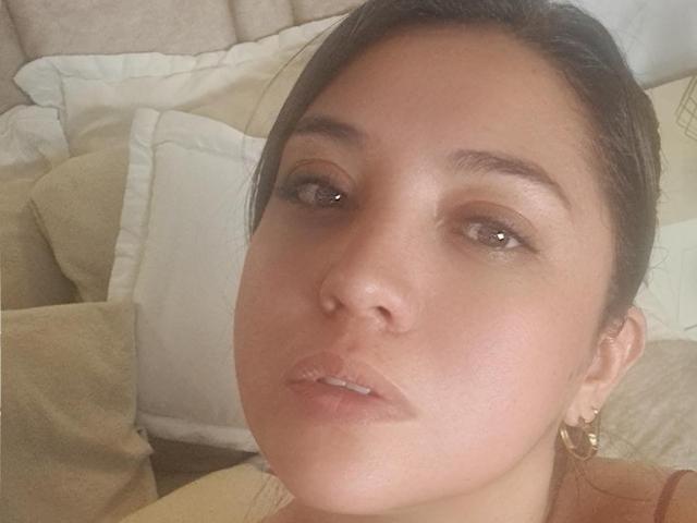 PaulaAnd has a light skin tone, brown eyes, and dark brown hair in a ponytail. She's wearing hoop earrings and has subtle makeup with glossy lips.