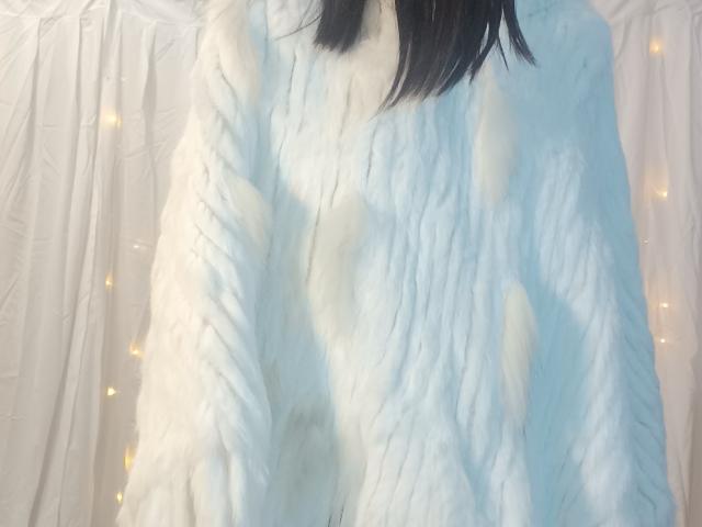 OrianaLaFrancaise trägt einen flauschigen weißen Pullover, wobei ihr schwarzes Haar teilweise sichtbar ist. Im Hintergrund sind sanfte, gelbe Lichterketten angebracht. Ihre Brüste sind klein und bedeckt..