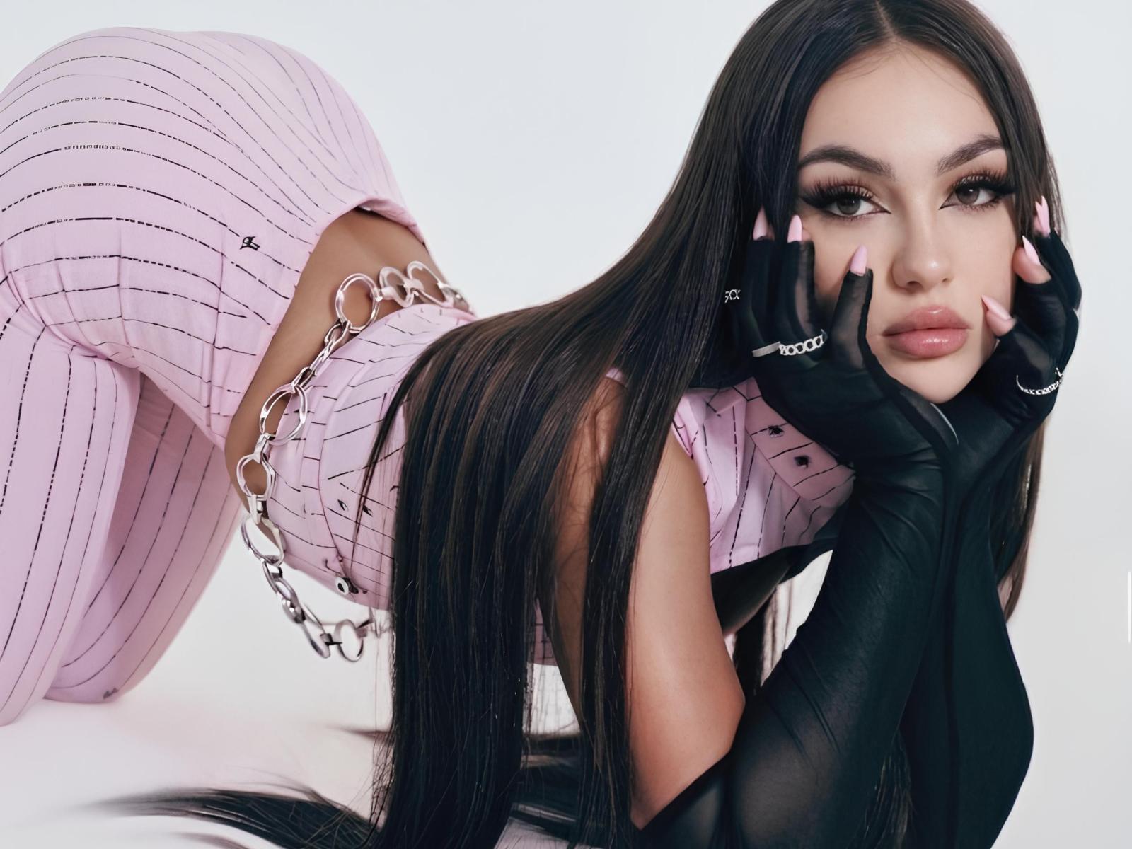 OdessaSerban with long black hair, pink striped pants, black gloves, and chain belt, on knees, hands on face, looking at camera, pink nails, seductive expression, tight ass, cute.