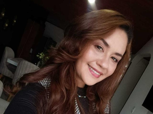 TheresaLarson with wavy brown hair, smiling, showing her pink lipstick and white teeth. She's wearing a black and silver top, looking cute and sexy.