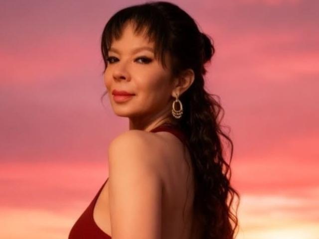 SamaraBellet ha lunghi capelli scuri e ondulati, rossetto rosso, e indossa un abito rosso, con la schiena rivolta verso la fotocamera, guardando oltre la spalla con un leggero sorriso..