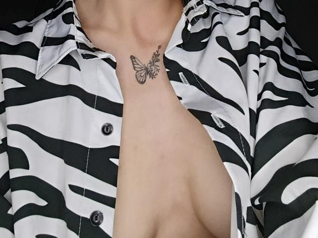 LissyLuxe's neck with a butterfly tattoo, wearing a zebra-patterned shirt, open to show her bare chest and collarbone. Her shirt buttons are black.