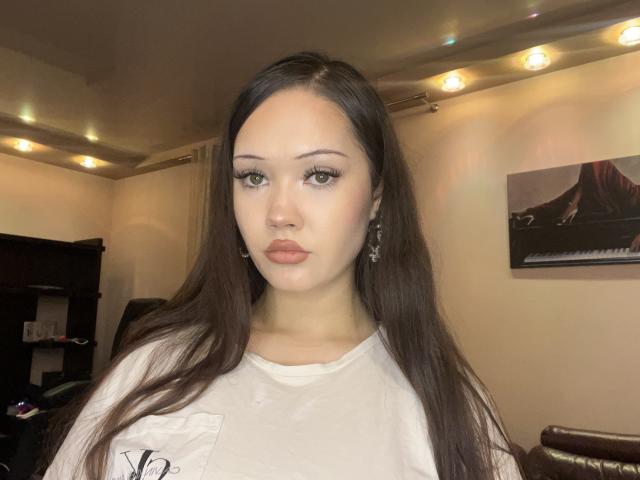 Lakendra Eytcheson, avec de longs cheveux bruns, portant une chemise blanche, a des lèvres roses et fines et des yeux verts, et porte des boucles d'oreilles, dans une pièce avec des guirlandes lumineuses..