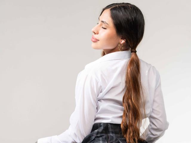 AntonellaReed with eyes closed, white shirt, black skirt, long brown ponytail, hoop earrings, slightly turned back, smiling, soft light, smooth skin, subtle makeup, relaxed pose.