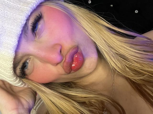 ShantalSummer with blonde hair, pink blush, and glossy red lips, pouting and wearing a white knit hat, has a cute, sexy face with blue eyes and long eyelashes.