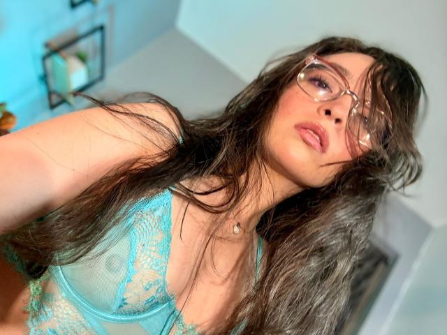 EvaMcAllister, avec de longs cheveux bruns, des lunettes, et un soutien-gorge en dentelle bleu qui révèle de petites seins et des mamelons. Elle regarde vers le haut, les lèvres roses entrouvertes, dans un autoportrait légèrement flou..