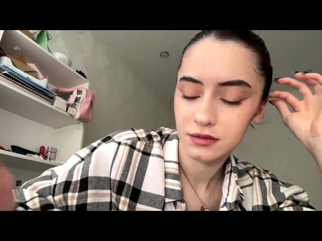TawnaCotto with closed eyes, plaid shirt, and hair tied back, showing off her tits with a subtle smile and a hand touching her ear. She's wearing a necklace.