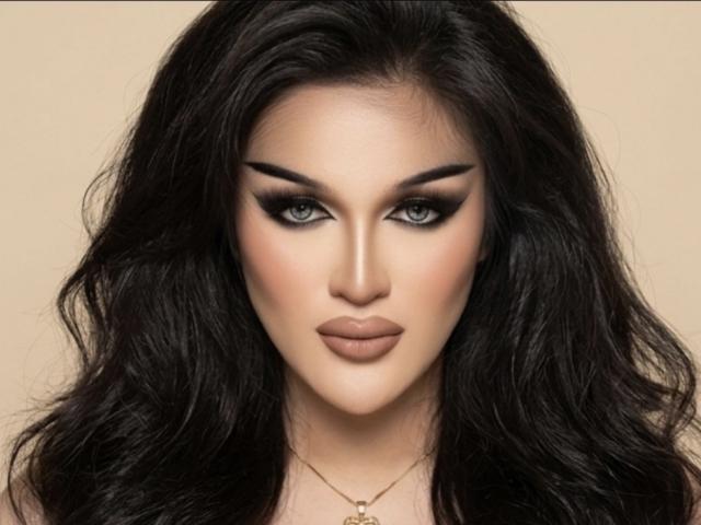 ChalanieFoxy with dark wavy hair, smoky eye makeup, and full lips, wearing a gold necklace, has a serious, sexy, and attractive face.