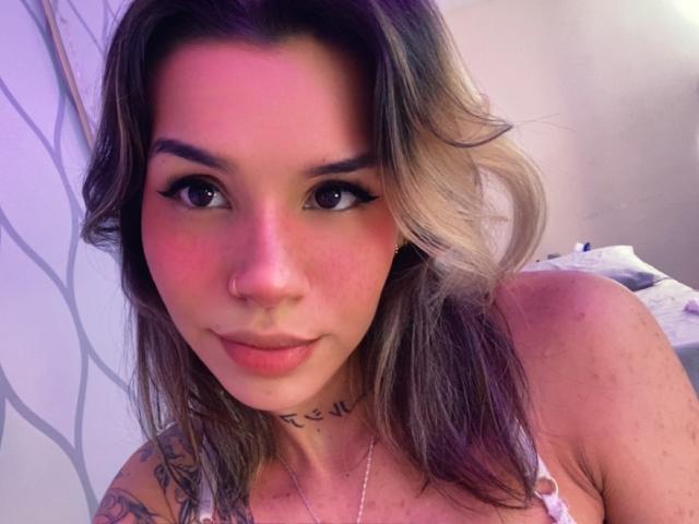 LenaBranch hat rosafarbene Wangen, schwarzen Eyeliner, einen Nasenring und ein Tattoo im Nacken. Sie schaut mit einem leichten Lächeln in die Kamera und trägt ein pinkes Oberteil..
