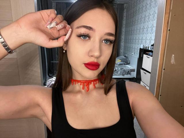 XeniaSherod with red choker, black tank top, red lipstick, and long brown hair, holding her ear with a silver ring, showing off her tits and sexy face.