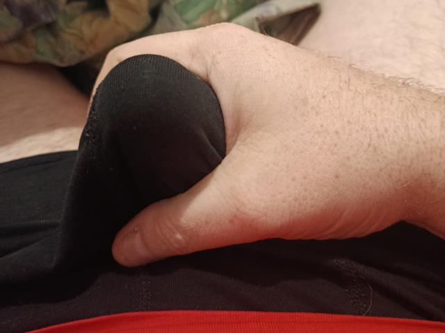 Floww69s Hand umklammert eine schwarze, stoffbezogene Stelle an den Gesäßbacken. Floww69s blasse, behaarte, leicht faltige Hand hält den schwarzen Stoff über einem roten Tuch..