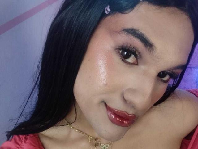 PamelaXFox with shiny, glossy red lips, black hair, and a gold necklace, smiling at the camera, showing off her cute face and subtle makeup.