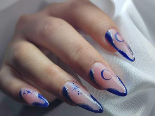 AsleyLoren's nails are long, almond-shaped, and painted with a clear base, blue tips, and blue crescent moon and star designs on each nail. Her hand is visible.