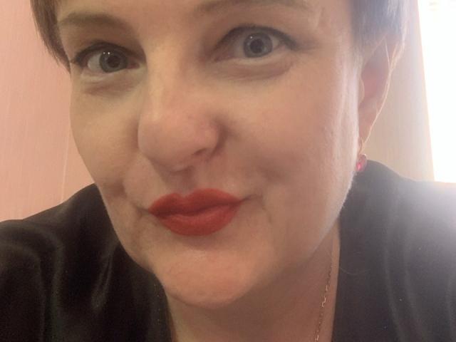 Margie Evans, con i capelli castani corti, gli occhi azzurri e il rossetto rosso acceso, indossa una maglietta nera, ha un viso leggermente gonfio e sorride dolcemente alla fotocamera..