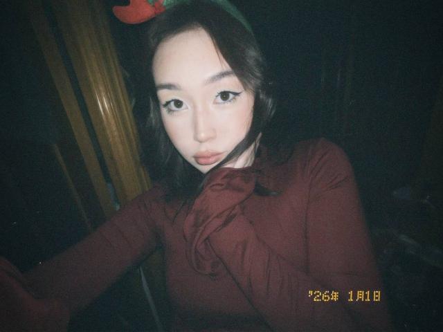 LorenzaMccaughan with dark hair, wearing a red top, has a pensive expression, hands near her face, and a green headband with a red bow, in a dimly lit room.