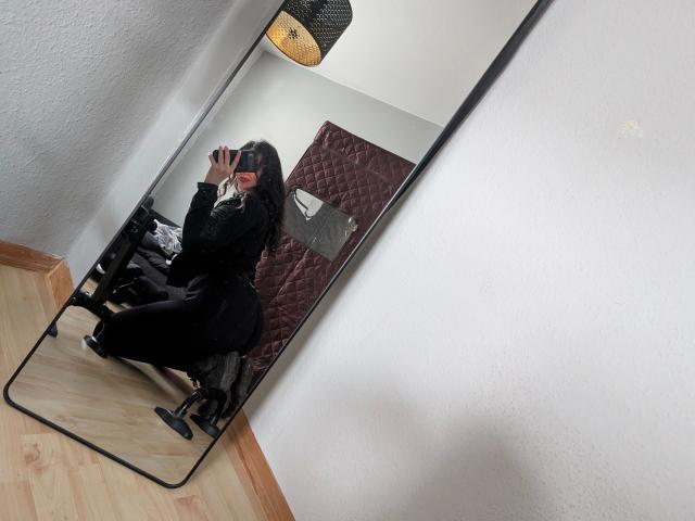 Jenna-sxy19-hot, squatting in front of a mirror, wearing black pants and a black top, taking a selfie with her phone, reflection shows her ass, in a room.