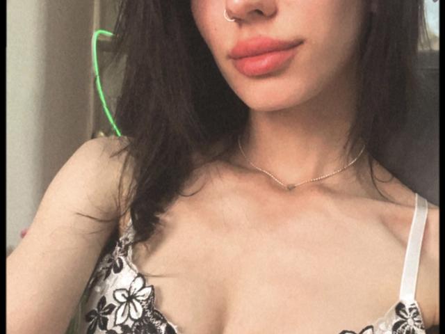 Valnes has brown hair, a nose ring, and pink lips. She's wearing a lace bra, showing her tits. She's also wearing a thin necklace. Her skin is light.