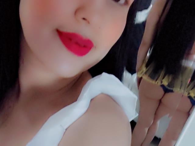 ValeriaRossii with red lips, white top, black hair, reflected in mirror showing her bare ass in yellow and black panties. Her face is in focus, her butt in reflection.