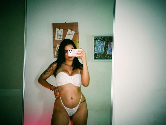 IsabellaJames with medium brown skin and black hair, wearing white lace bra and thong, showing her tits and pussy in a mirror selfie, hand on hip, tattoo on arm.