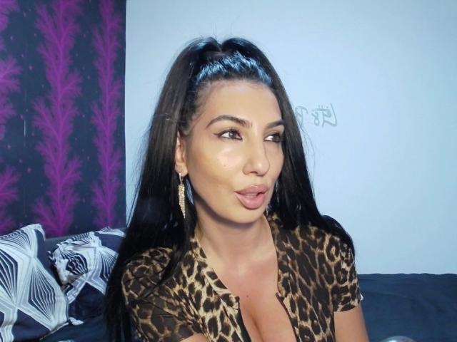 BrunetteBabe69 with long black hair in a high ponytail, wearing a leopard print shirt, pouting her pink lips, looking to the side, with gold earrings, showing her tits.
