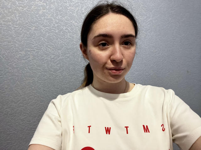 LigiaRobella has a cute face with light skin, brown eyes, and a slight smile. She's wearing a white shirt with red letters, and her brown hair is in a ponytail.