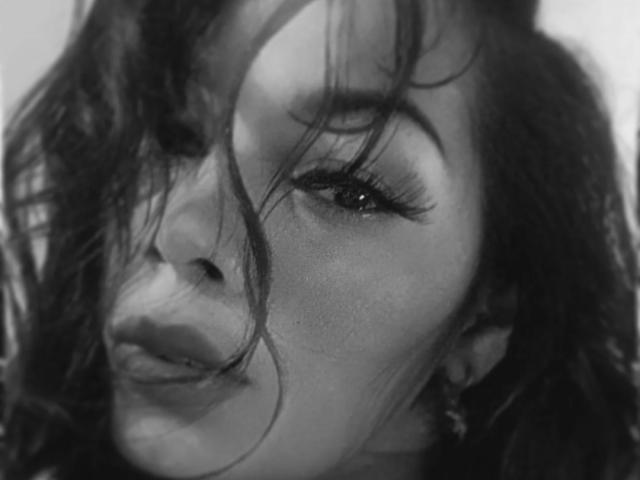 FetishLoverAna's face in black-and-white, her long, messy hair covering her eyes, full lips slightly parted, with prominent eyelashes and a subtle, seductive expression.