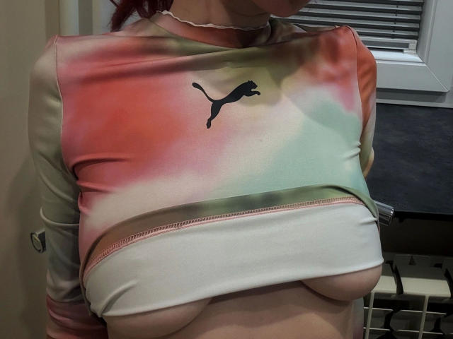 La colorida camiseta de Puma de EvyPink-hot se levanta, revelando sus pechos desnudos y sus pequeños pezones rosados pálidos. Lleva un collar rosa y tiene el pelo rojo..