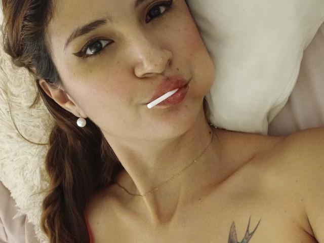AmeliaBlond a une cigarette dans sa bouche retroussée, des yeux marron avec un trait d'eye-liner, et un petit tatouage sur sa poitrine gauche. Elle porte des boucles d'oreilles de perles et un collier en or..