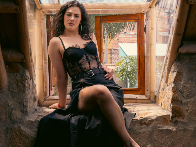 Elizabeth Dupont, avec ses cheveux noirs bouclés, son soutien-gorge en dentelle noire et sa jupe noire, assise dans un encadrement de fenêtre en pierre, sa main posée sur sa cuisse, laissant apparaître ses jambes nues et sa ceinture noire..