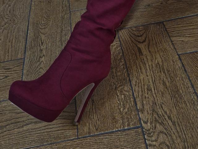 WenTina's maroon, high-heeled boot with a platform sole and white sole, resting on a wooden floor with visible grain patterns. Boot is slightly angled to the left.