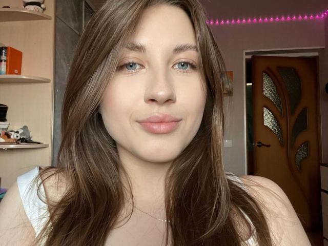 DremaEspina a la peau claire, les yeux bleus et les cheveux bruns, avec des lèvres roses dans un léger sourire. Elle porte un haut blanc sans manches, et ses seins sont légèrement visibles..