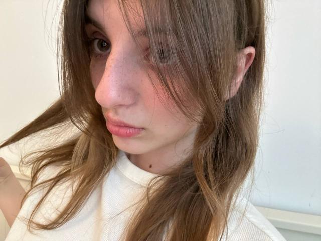 KarieMestler a les cheveux bruns, un nez rosâtre et des lèvres légèrement entrouvertes de couleur rose, elle porte une chemise blanche et a une expression sérieuse sur une photo en gros plan, avec un éclairage doux..