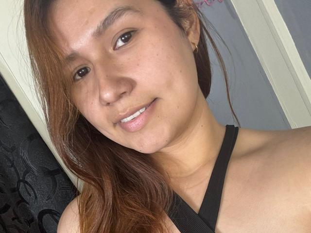 SofiaVelvet a un visage brun clair avec de longs cheveux bruns, des yeux bruns et un léger sourire, et elle porte un haut noir à bretelles qui laisse apparaître ses épaules nues..