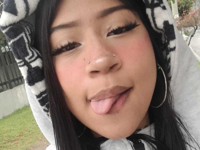 BonnieBodn with black hair, nose piercing, and hoop earrings, sticking out tongue, showing makeup, and large eyelashes, wearing a black and white hooded sweatshirt.