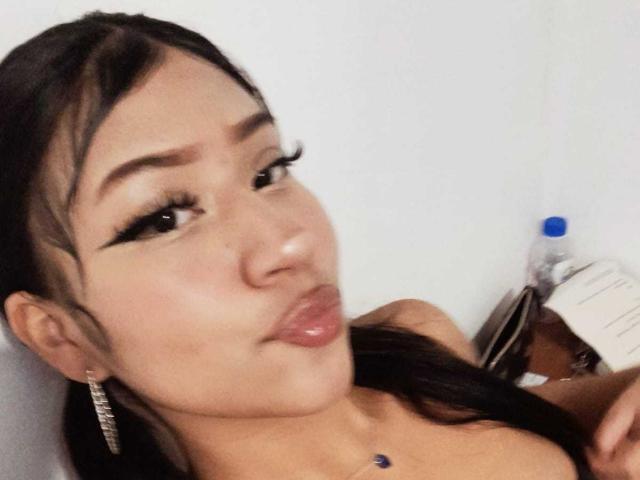 BonnieBodn tiene labios carnosos, delineador de ojos oscuro y pestañas largas, con un rostro lindo, ligeramente rechoncho y cabello oscuro, y lleva un collar con una gema azul. Está sosteniendo una botella de agua..