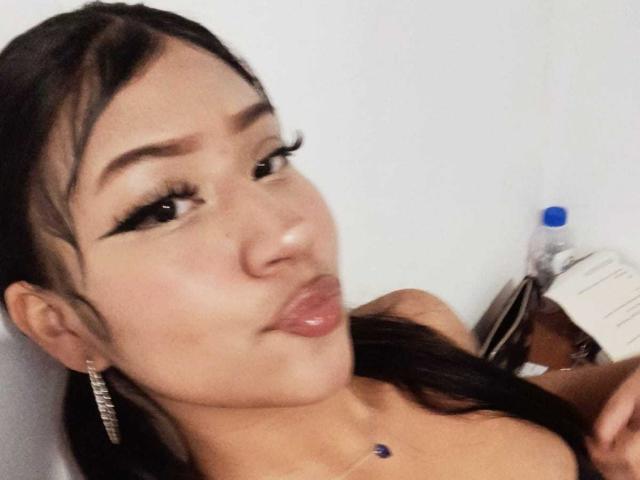 BonnieBodn has puffy, glossy lips, dark hair in a ponytail, and thick, long eyelashes. She's sticking out her tongue and wearing a blue jewel necklace.