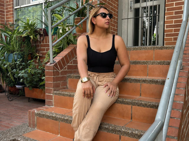 CristalWil with tan pants, black tank top, and black sunglasses, sitting on brick stairs. She's wearing a gold watch and has a curvy ass and medium tits.