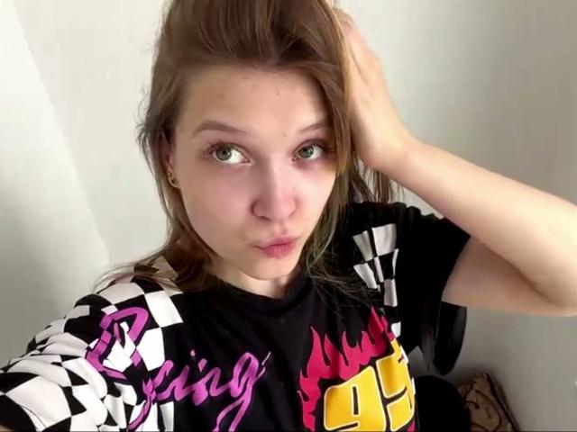 Vera Brabazon, con ojos verdes, labios carnosos y cabello castaño claro, vestida con una camisa negra a cuadros con llamas rosas y amarillas, con la mano en el pelo, mirando a la cámara..