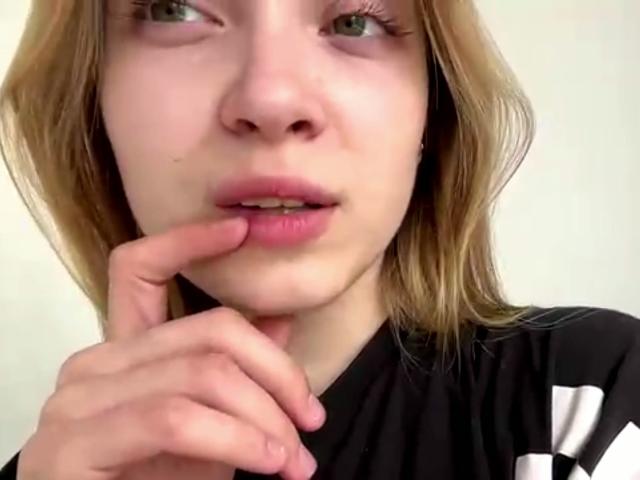 Vera Brabazons Gesicht mit hellbraunen Haaren, rosafarbenen Lippen und grünen Augen, die mit ihrem Zeigefinger ihre Unterlippe berührt, trägt ein schwarz-weißes Hemd..