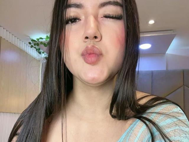 ScarlettVex with puffy pink lips, winking, and her long dark hair, wearing a striped blue top, showing off her soft tits and cute ass in a selfie.