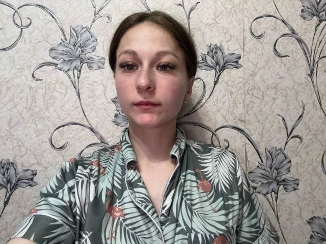 Cherelle Delozier, mit braunen Haaren, trägt ein grünes, geblümtes Hemd und hat einen neutralen Gesichtsausdruck, helle Haut, eine kleine Nase und braune Augen. Sie steht vor einer Tapete mit Blumenmuster..