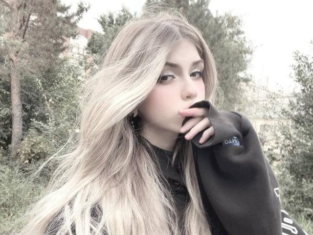 LauraleePenderel with long blonde hair, black hoodie, and finger in mouth, looking slightly to the side. She has light makeup, green eyes, and a cute, sexy face.