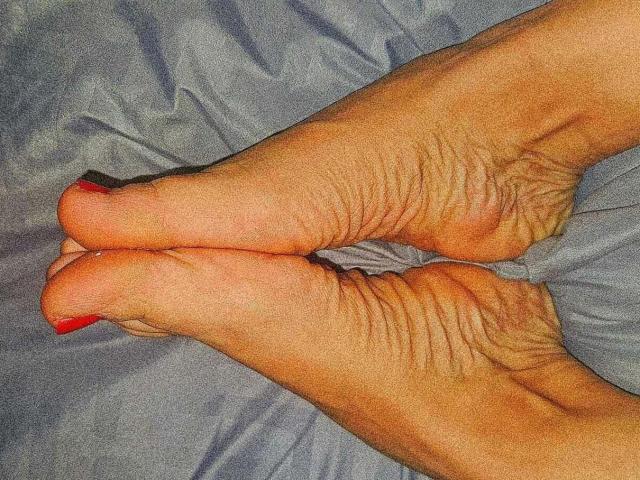CoupleHottX69's feet, showing wrinkled soles and red-painted toenails, are crossed and reflected in a mirror. The reflection is centered below the actual feet.