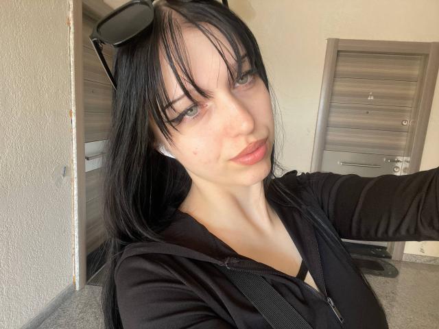 AmaiRin, com cabelo preto, olhos verdes e pele clara, vestindo um moletom preto, tem os lábios levemente entreabertos e óculos de sol pretos na cabeça, em um selfie..