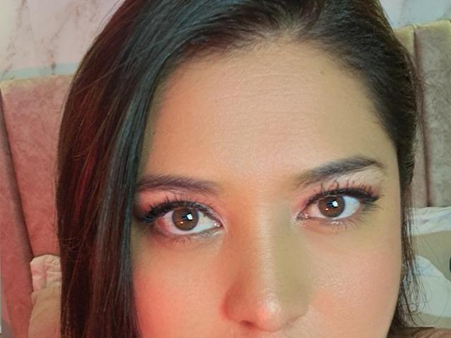 PaulaAnd's face with brown eyes, long dark brown hair, and subtle makeup, showing her eyelashes and slightly parted full lips. Her skin is smooth and she has a cute nose.