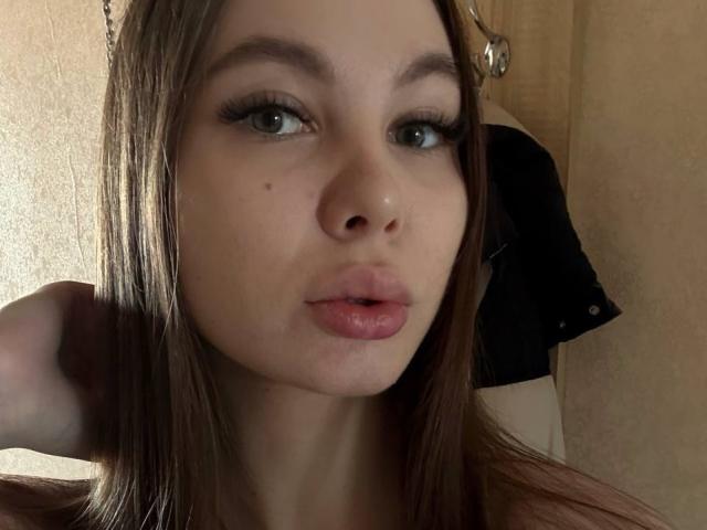 Karleen Tallas heeft bruin haar, groene ogen en roze lippen, met een kleine moedervlek op haar linkerwang. Ze kijkt naar de camera met een lichte frons, haar hand in haar haar..