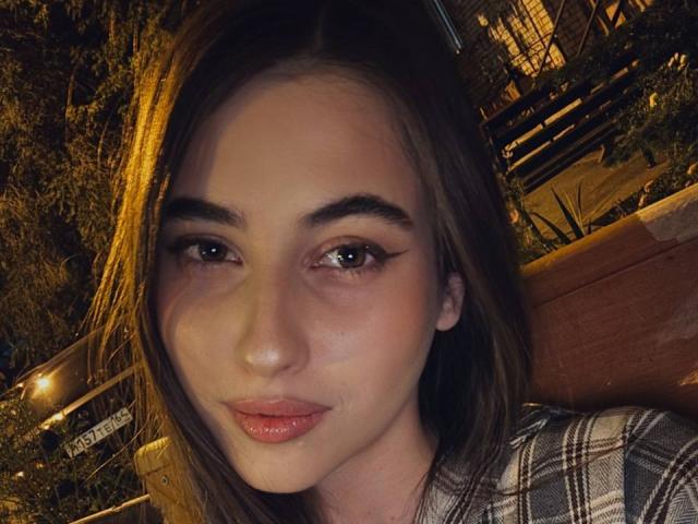 LateshaLuckenbaugh has light skin, brown eyes with winged eyeliner, pink glossy lips, and straight brown hair. She's wearing a plaid shirt, looking cute and sexy.