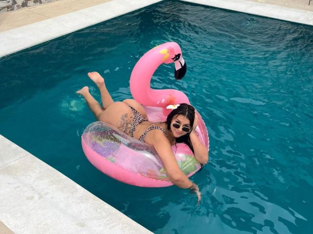 AlessiaFerry lies on a pink flamingo inflatable in a pool, wearing a leopard print bikini, showing her ass, and her tattooed back, with a flower in her hair.
